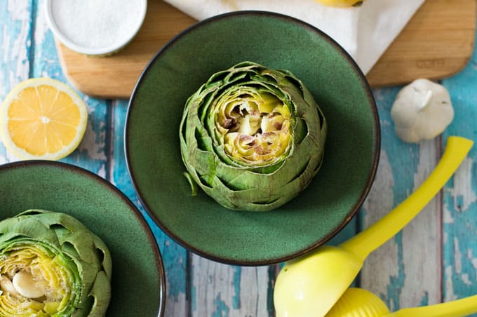 Closeup of artichokes in bowls with a citrus squeezer, lemon, and garlic.