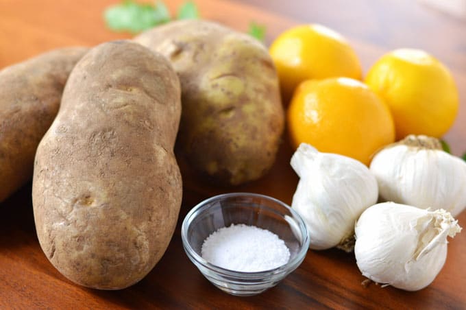 Potatoes, lemons, garlic bulbs, and a bowl of salt on a tabletop.