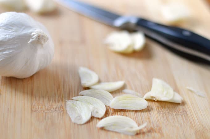 Sliced garlic on a cutting board with a pairing knife.