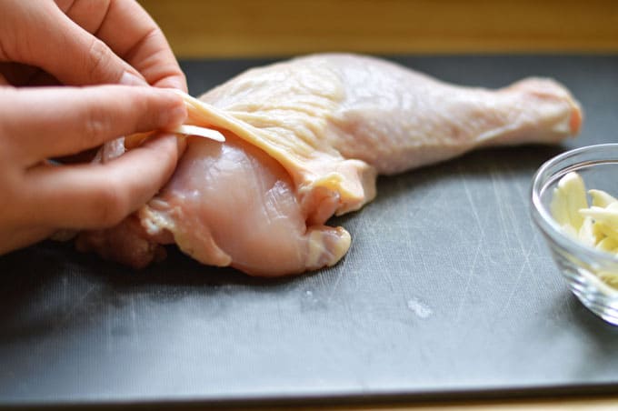A slice of garlic being placed on a chicken leg.