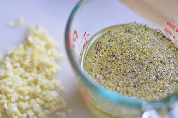 A close up of vinaigrette in a measuring glass with chopped garlic next to it.