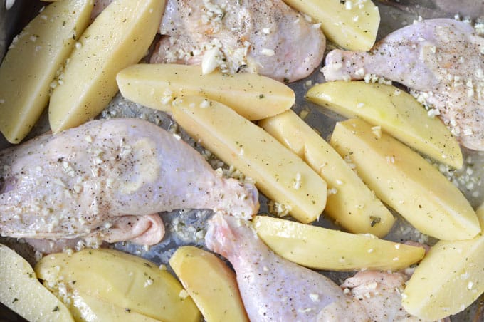 Pieces of chicken legs and potatoes coated in garlic in a baking pan.