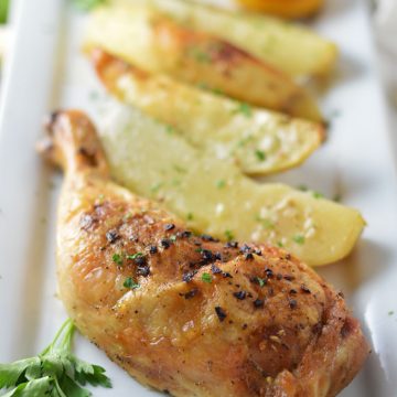 A close up of roasted chicken and potatoes on a plate.