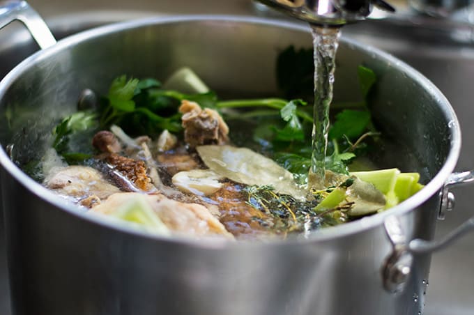 Water filling up a pot full of chicken stock ingredients.