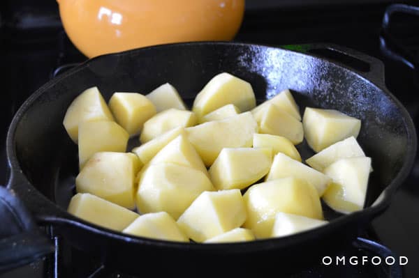 Raw potato pieces cooking in a skillet.
