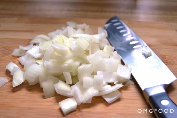 Chopped onion and a chef\'s knife on a cutting board.