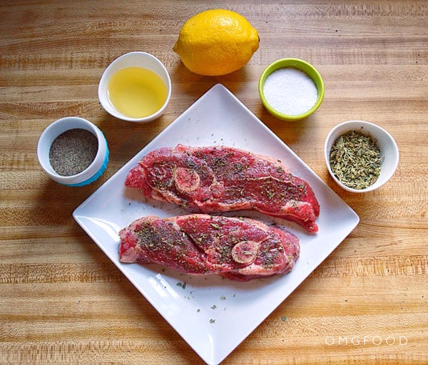 A plate of raw lamb chops surrounded by oil, lemon, and spices.