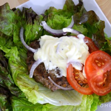 Closeup of a burger patty on a bed of lettuce topped with mayo.