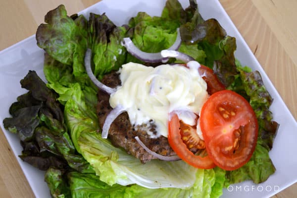 Closeup of a burger patty on a bed of lettuce topped with mayo.