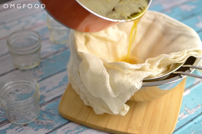 Melted butter being poured through a cheesecloth lined mesh strainer into a bowl.