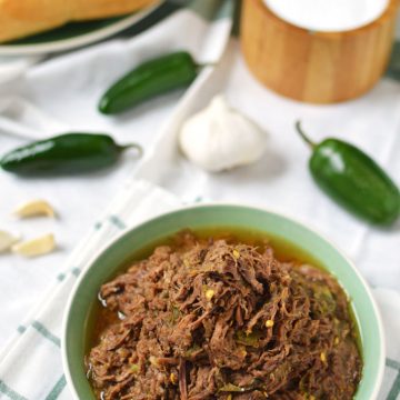 A bowl of shredded beef with jalapeños and garlic in the background.