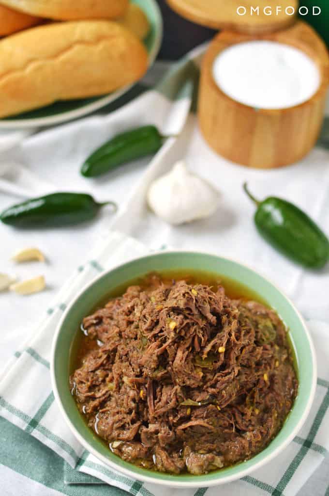 A bowl of shredded beef with jalapeños and garlic in the background.