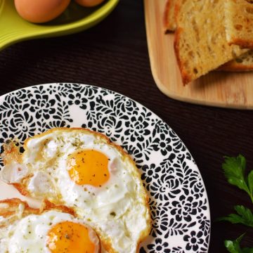 Fried eggs on a plate with toast in the background.