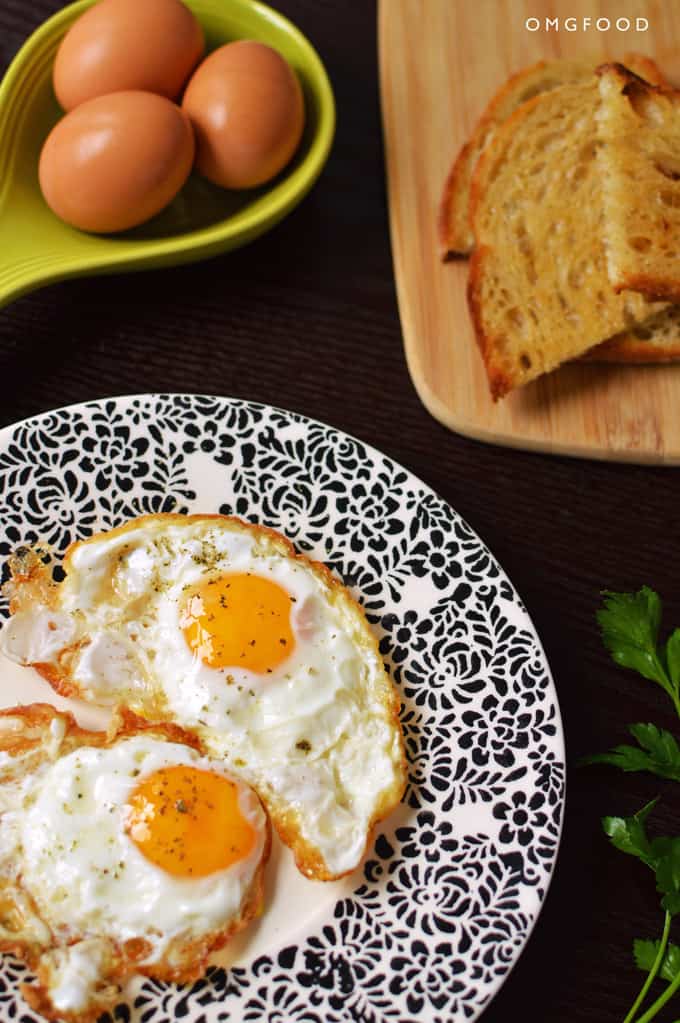 Fried eggs on a plate with toast in the background.