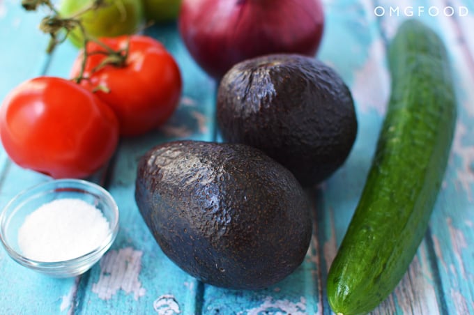 Closeup of avocados, tomatoes, cucumber, and red onion.