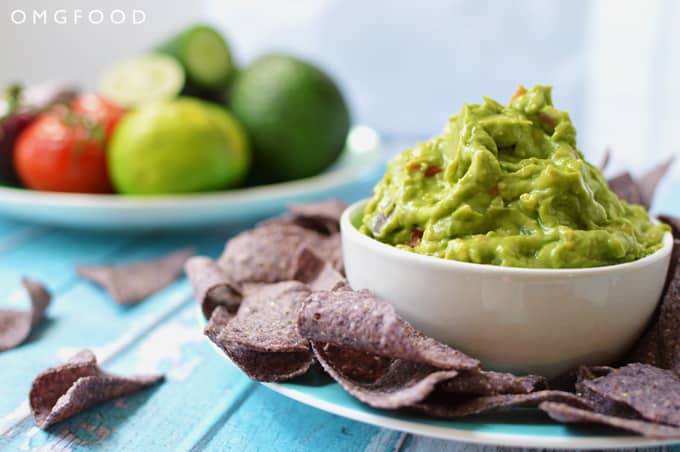 A bowl of guacamole on a plate with tortilla chips.