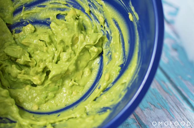 Closeup of mashed avocado in a blue bowl.