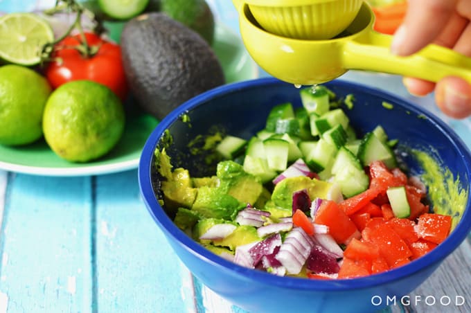 Lime being squeezed into a bowl of guacamole ingredients.