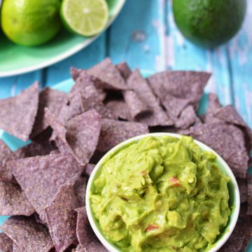 A plate of chips and bowl of guacamole on a tabletop.