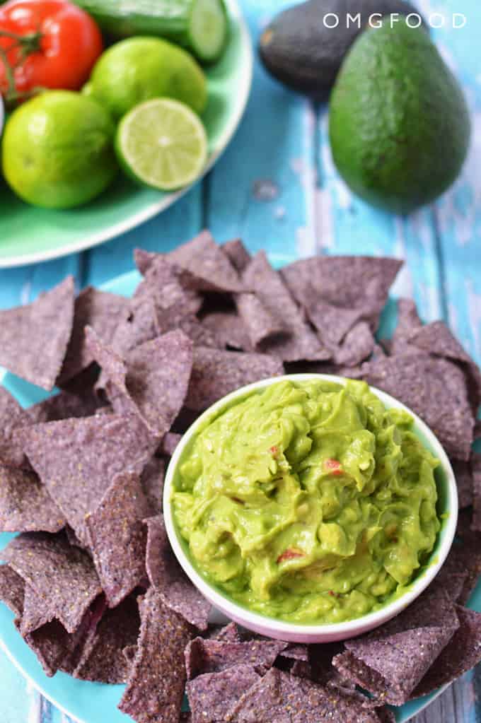 A plate of chips and bowl of guacamole on a tabletop.