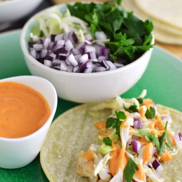 A fish taco on a plate with a side of sauce and assorted toppings.