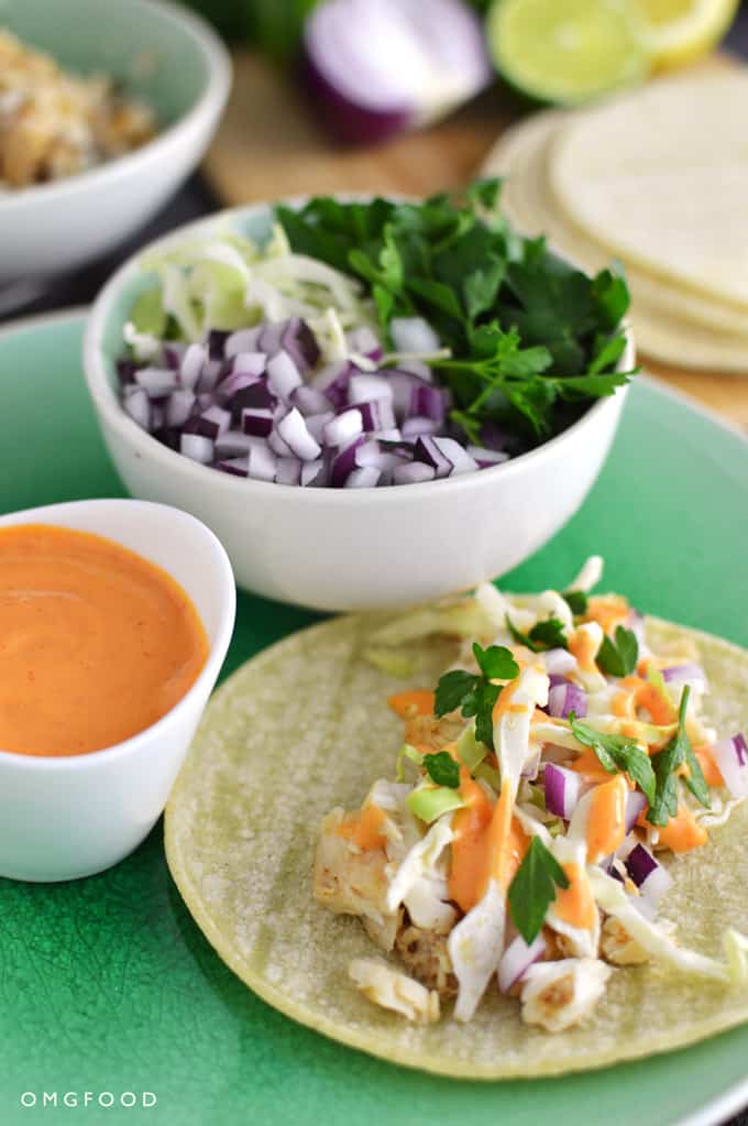 A fish taco on a plate with a side of sauce and assorted toppings.