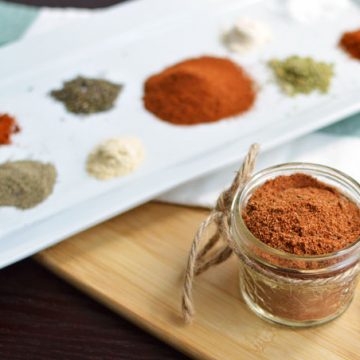 A jar of cajun spice blend with a plate of spices.