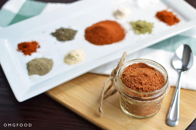 A jar of cajun spice blend with a plate of spices.