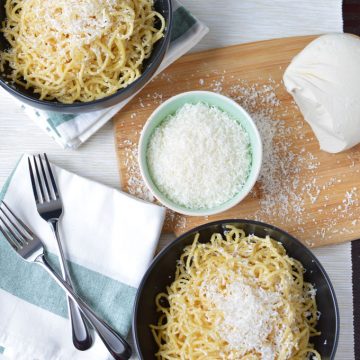 Bowls of spaghetti and grated cheese on a tabletop.