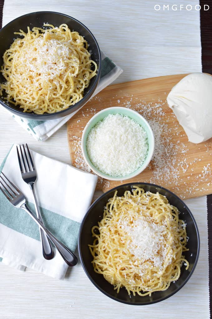 Bowls of spaghetti and grated cheese on a tabletop.