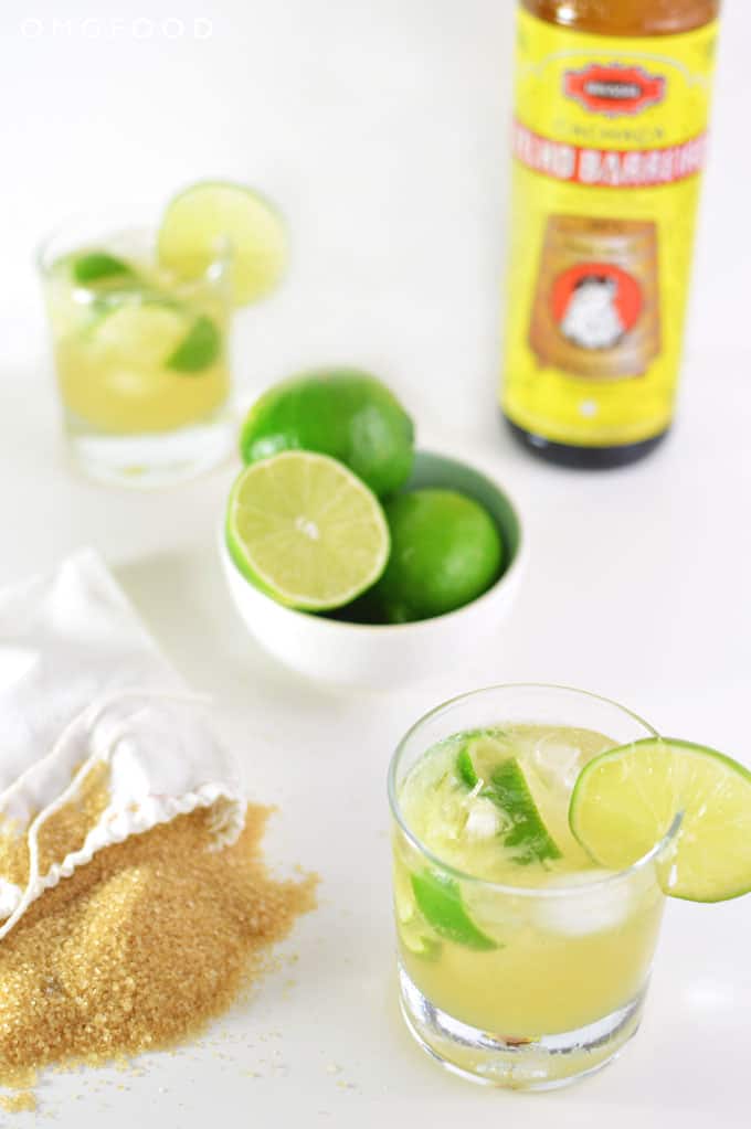 A bowl of limes, bag of sugar, and cocktails on a tabletop.