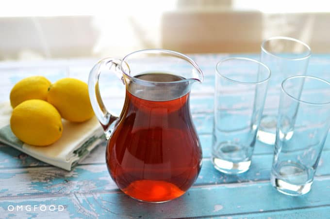 A small pitcher of iced tea next to lemons and empty drinking glasses.