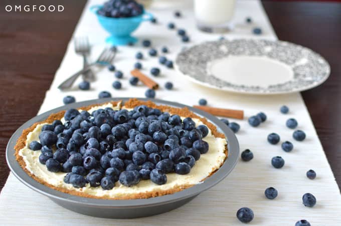 Blueberry cream pie on a tabletop with forks, a plate, and blueberries in the background.