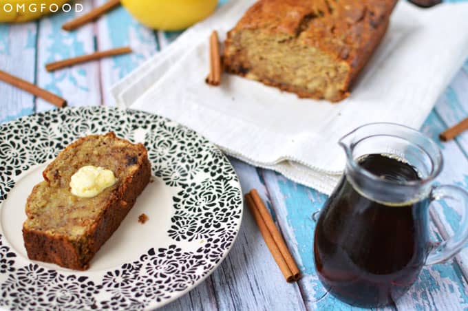 A slice of toasted banana bread with butter on a plate with a loaf of banana bread in the background.