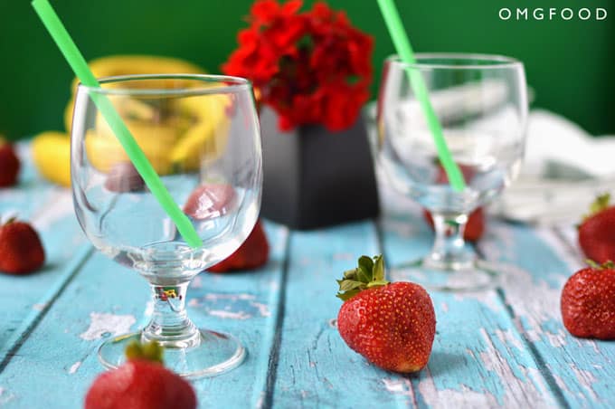 Empty drinking glasses next to strawberries and a small vase of red flowers.