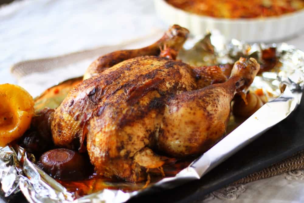 Closeup of a whole cooked chicken on a foil-lined platter.