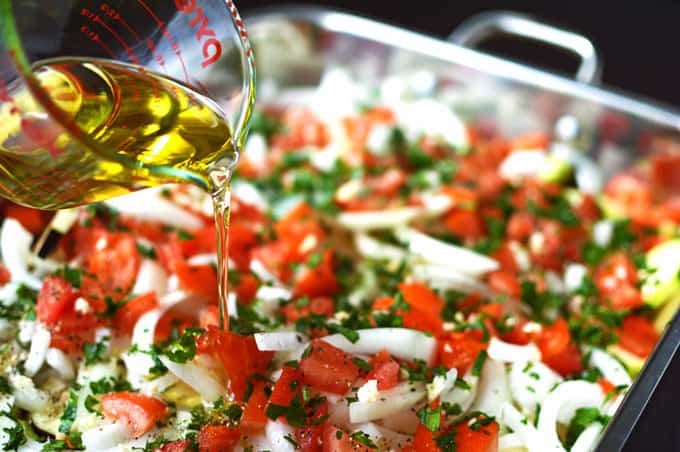 Olive oil pouring into a large pan of mixed vegetables.