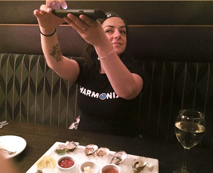 A woman sitting at a table taking a photo of food.