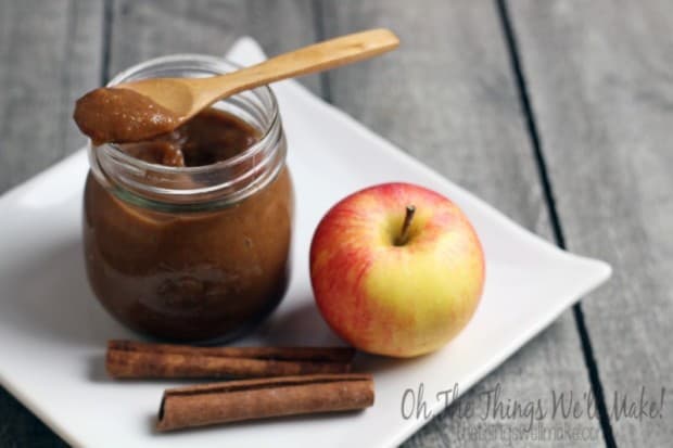 A jar of apple butter on a plate with an apple and cinnamon sticks.