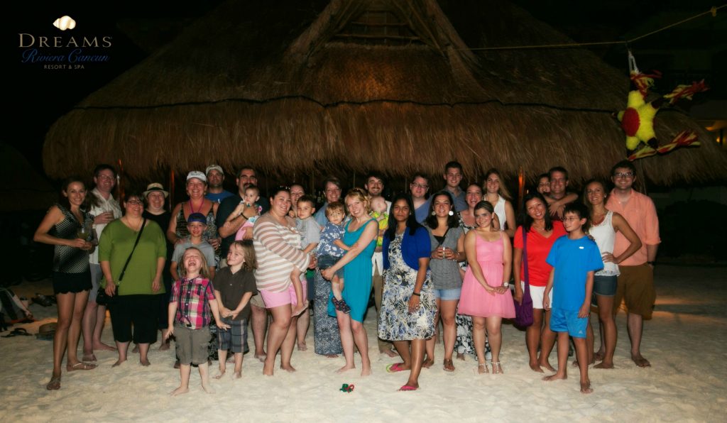 A group of people standing on a beach in front of a hut.