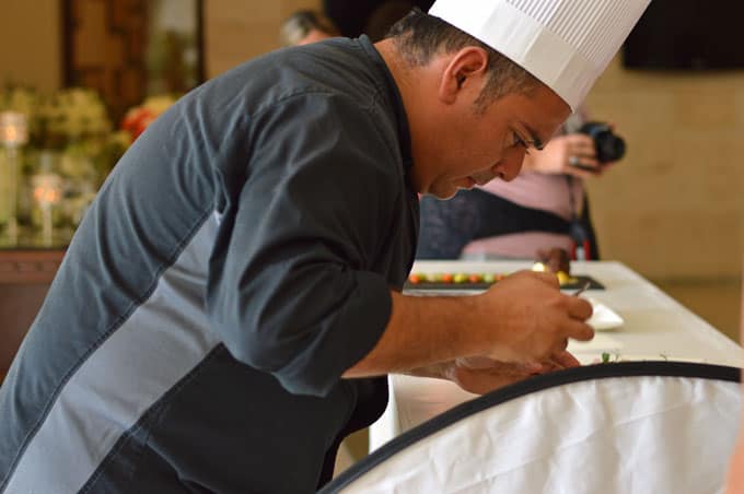 A chef styling a plate next to a photo reflector.