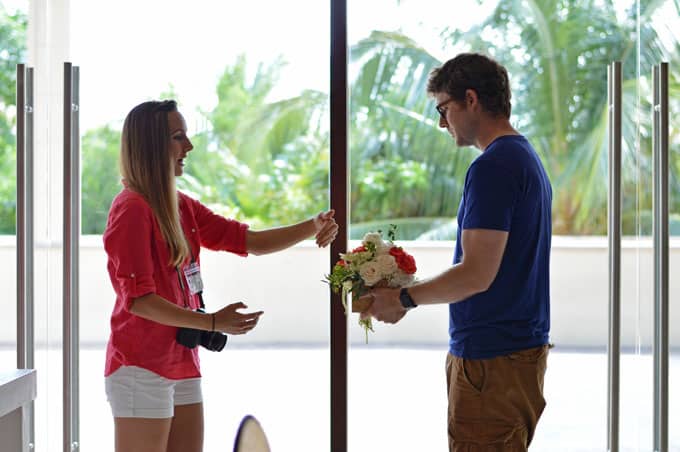 A woman with a camera and man with a bouquet of flowers standing next to a window.