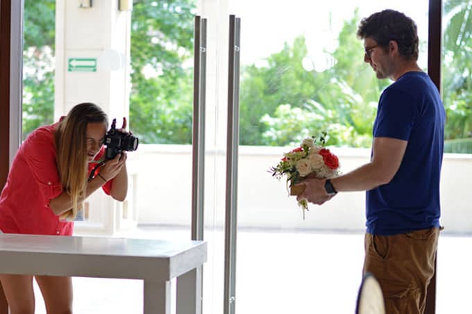 A woman taking a photo of a man holding a bouquet of flowers.