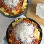 Bowls of pasta topped with meat sauce and grated cheese.
