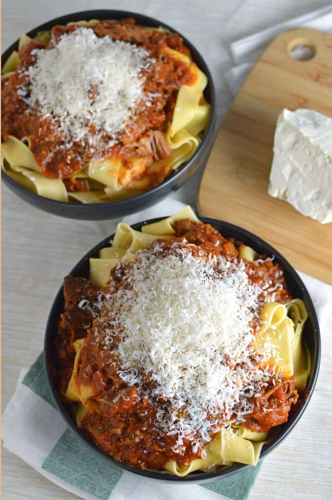 Bowls of pasta topped with meat sauce and grated cheese.