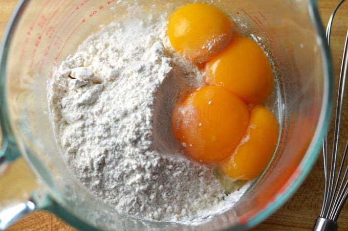 Closeup of egg yolks and flour in a measuring bowl.