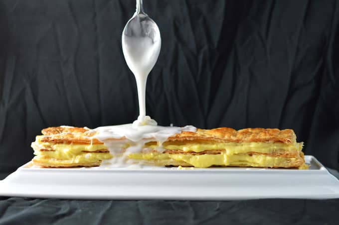 A spoon dripping icing onto puff pastry.