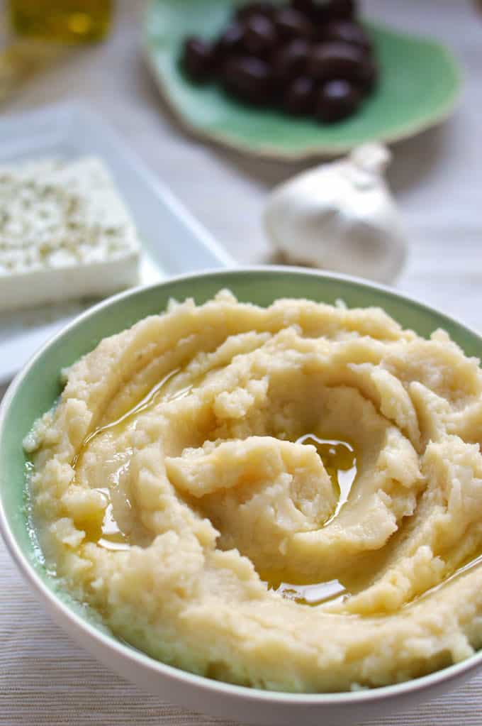 Whipped potato dip in a bowl with garlic and feta in the background.