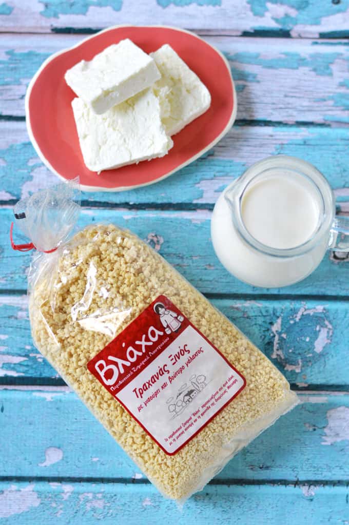 A plate of sliced feta, jug of milk, and package of trahana grains on a tabletop.