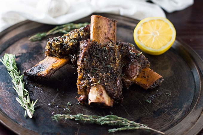 Roasted beef ribs on a platter with herbs and lemon.